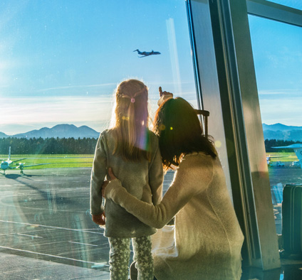 Mother and daughter looking at a starting airplane from the airport building, Sustainable Aviation Fuel (photo)