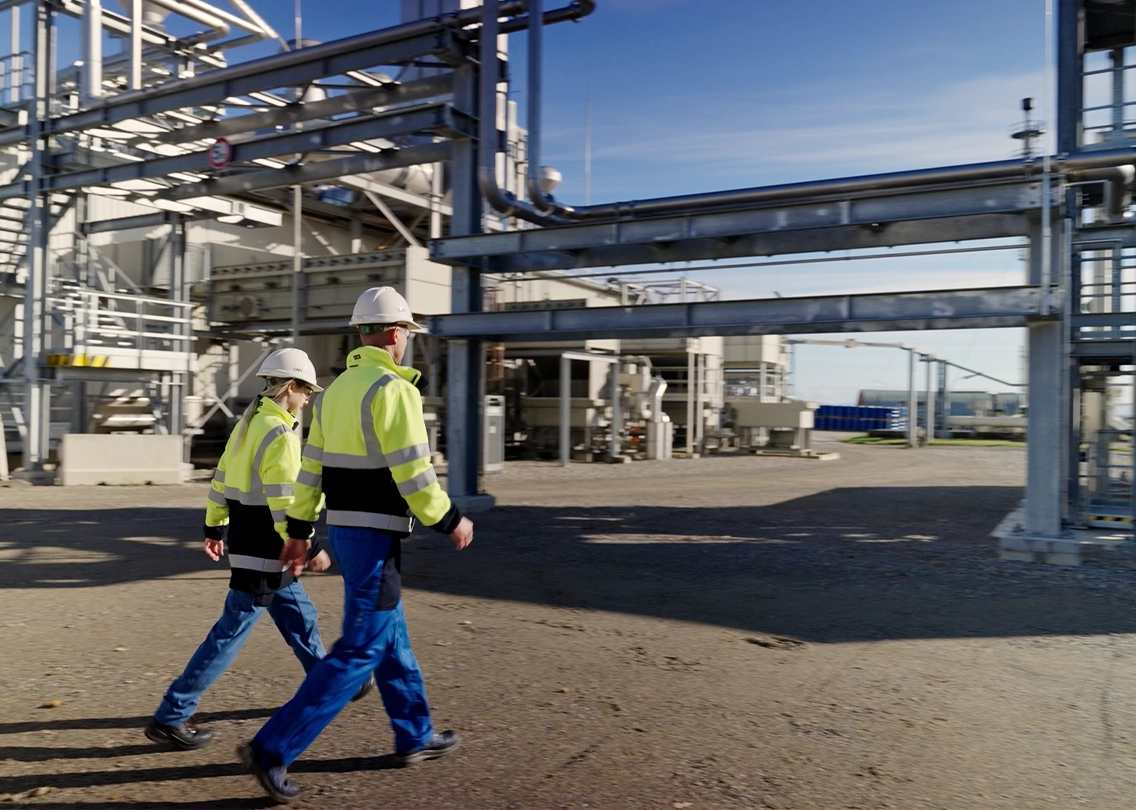 Eine Frau und ein Mann (zwei OMV-Mitarbeiter:innen) auf einem Werksgelände (Foto)