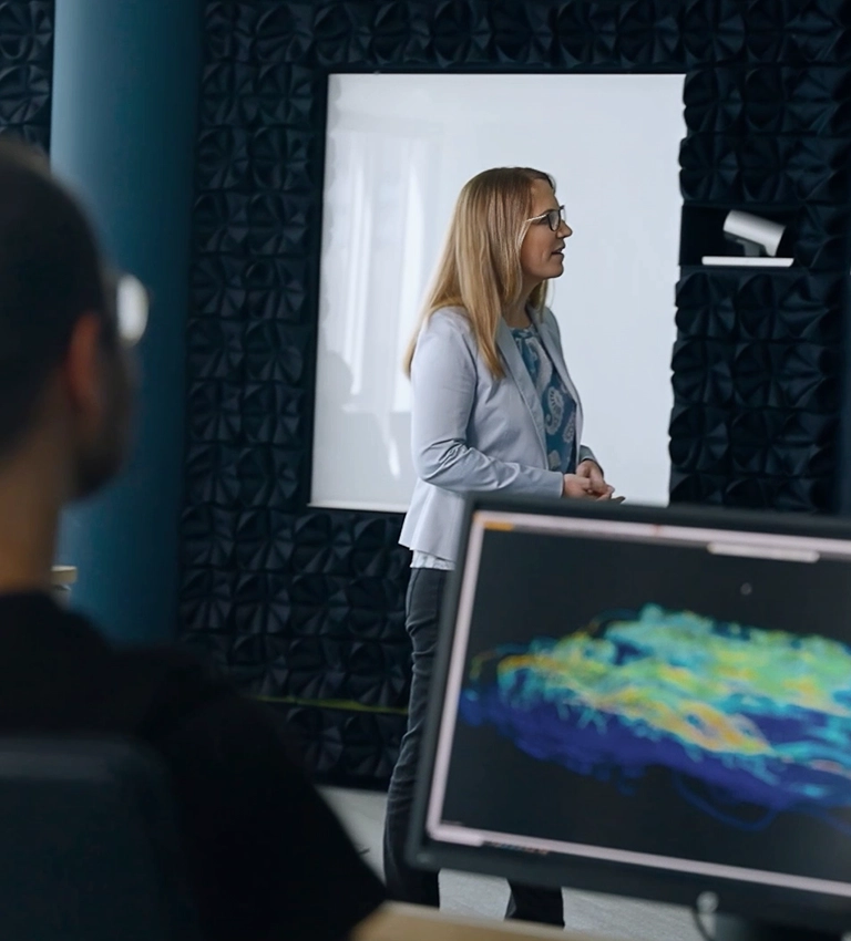 A woman in front of a screen presenting, a man sitting in front of his PC turned towards the woman (photo)