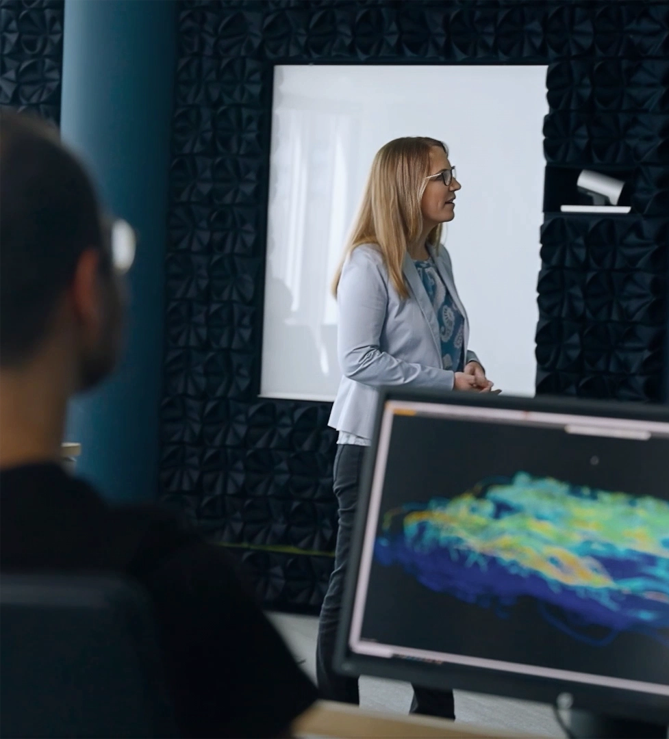 A woman in front of a screen presenting, a man sitting in front of his PC turned towards the woman (photo)